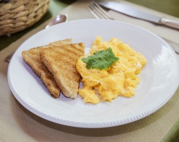 Desayuno con huevos revueltos cremosos y tostadas de pan integral, decorado con hoja de cilantro.